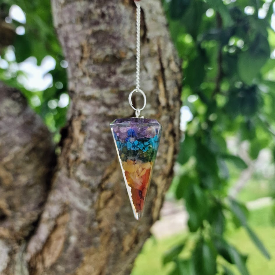 Colourful chakra resin pendulum with embedded stones and a silver chain featuring seven chakra crystal beads for energy healing and spiritual alignment.