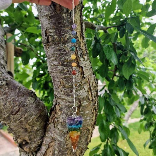 Colourful chakra resin pendulum with embedded stones and a silver chain featuring seven chakra crystal beads for energy healing and spiritual alignment.