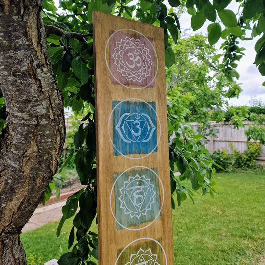Hand-painted chakra wall art on natural wood, featuring seven chakra symbols in vibrant colours