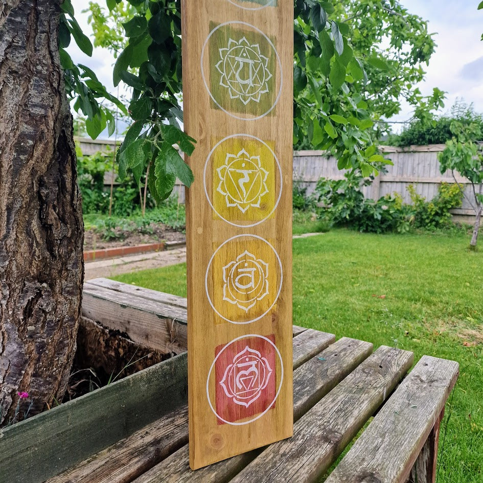 Hand-painted chakra wall art on natural wood, featuring seven chakra symbols in vibrant colours