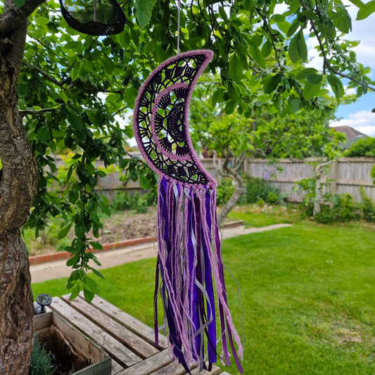 Handmade crochet Moon dreamcatcher with purple and pink ribbons and fringe, perfect for boho wall décor and nursery spaces.