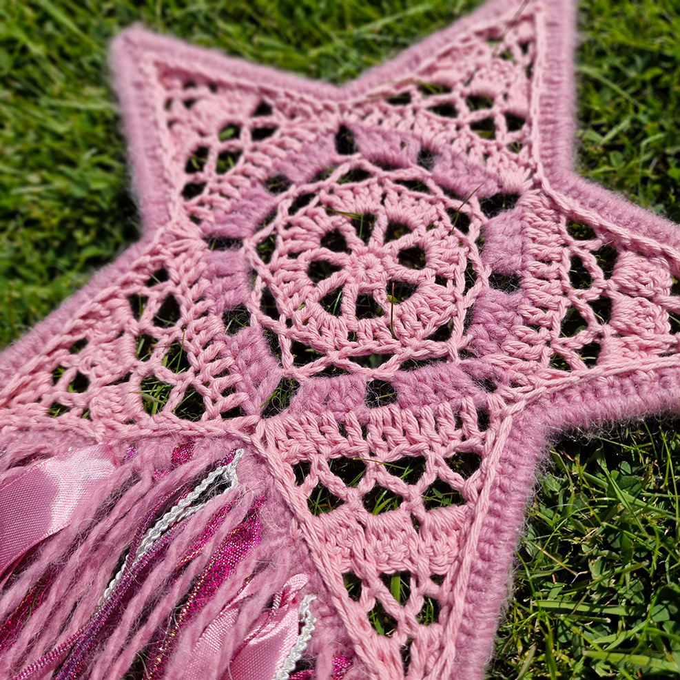 Handmade crochet star dreamcatcher with pink and silver ribbons and fringe, perfect for boho wall décor and nursery spaces.
