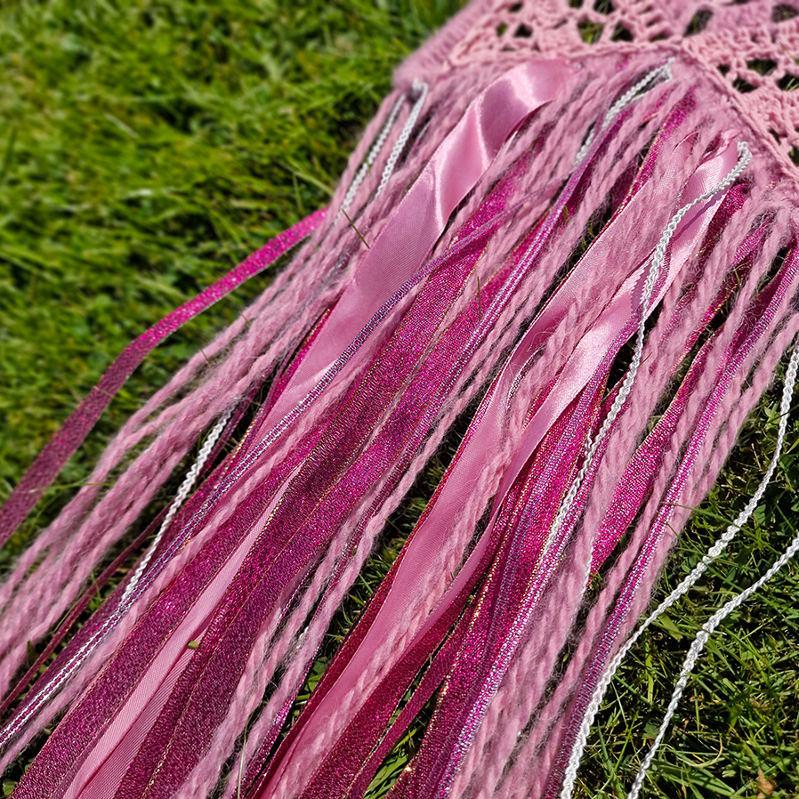 Handmade crochet star dreamcatcher with pink and silver ribbons and fringe, perfect for boho wall décor and nursery spaces.