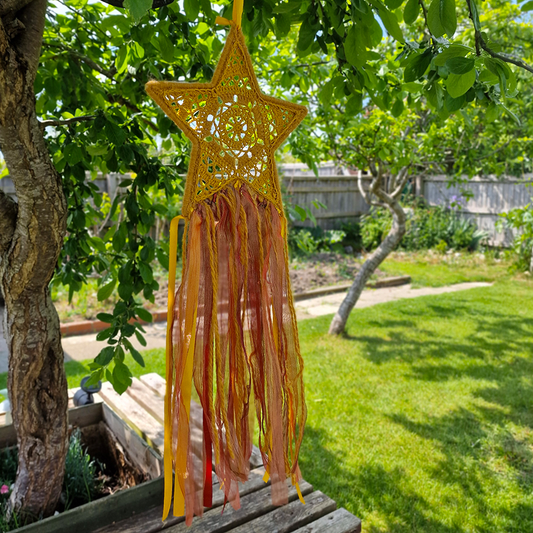 Handmade crochet star dreamcatcher with yellow, orange and brown ribbons and fringe, perfect for boho wall décor and nursery spaces.