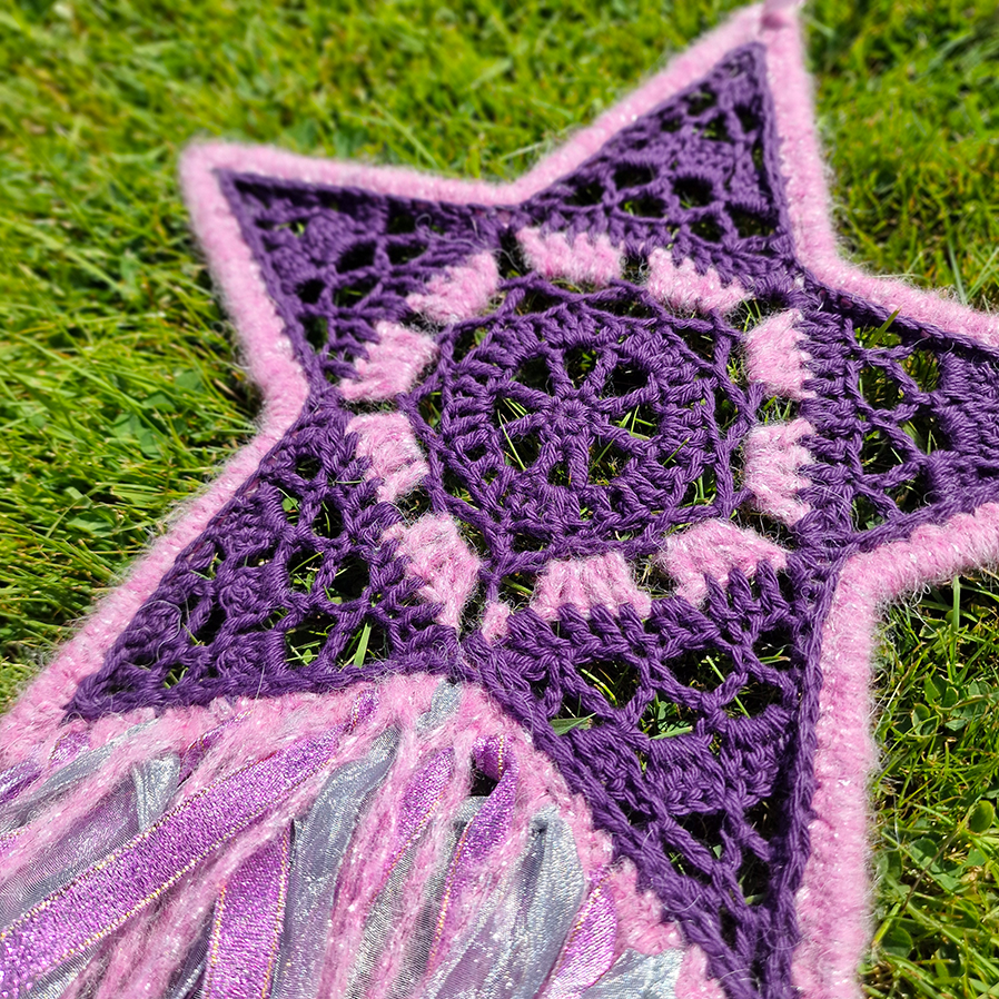 Handmade crochet star dreamcatcher with purple and pink ribbons and fringe, perfect for boho wall décor and nursery spaces.