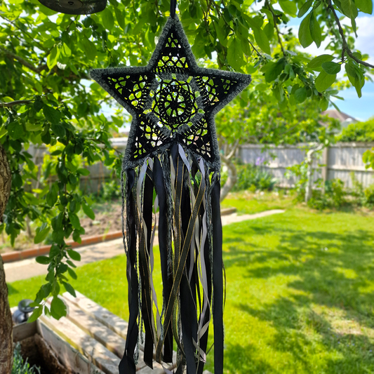 Handmade crochet star dreamcatcher with black, grey and silver/gold ribbons and fringe, perfect for boho wall décor and nursery spaces.
