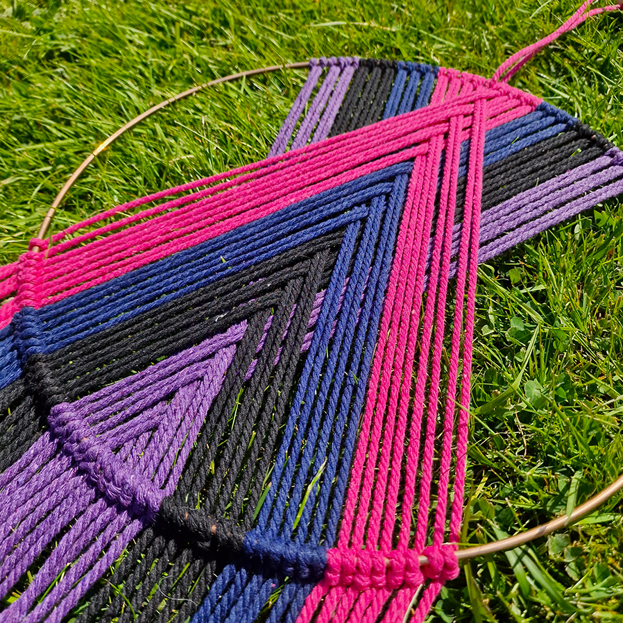 Handcrafted geometric macramé wall hanging in purple, pink, blue and black colours with beads for boho décor