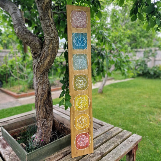 Hand-painted chakra wall art on natural wood, featuring seven chakra symbols in vibrant colours