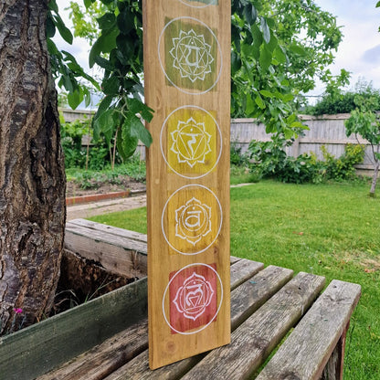 Hand-painted chakra wall art on natural wood, featuring seven chakra symbols in vibrant colours