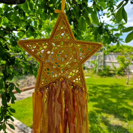 Handmade crochet star dreamcatcher with yellow, orange and brown ribbons and fringe, perfect for boho wall décor and nursery spaces.