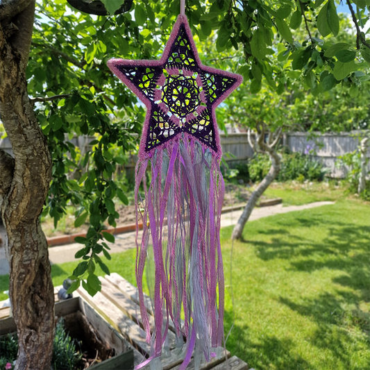 Handmade crochet star dreamcatcher with purple and pink ribbons and fringe, perfect for boho wall décor and nursery spaces.