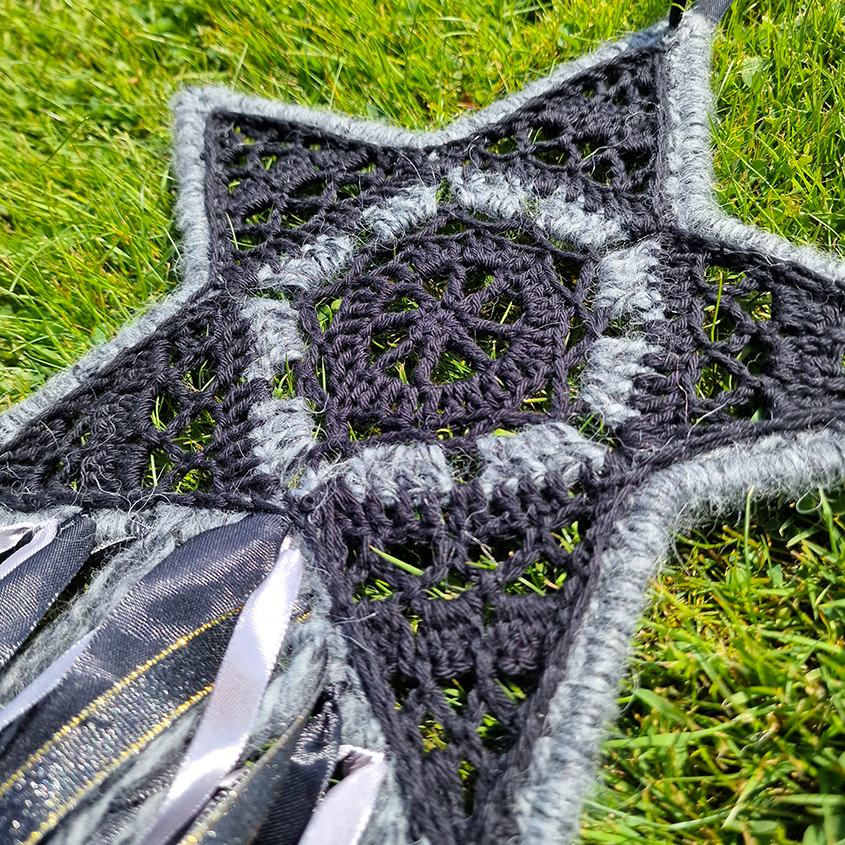 Handmade crochet star dreamcatcher with black, grey and silver/gold ribbons and fringe, perfect for boho wall décor and nursery spaces.