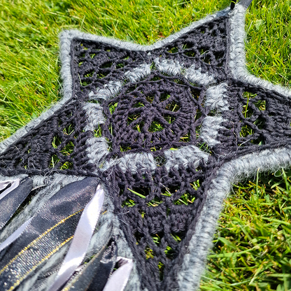 Handmade crochet star dreamcatcher with black, grey and silver/gold ribbons and fringe, perfect for boho wall décor and nursery spaces.